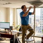 Technician adjusting HVAC vent in office